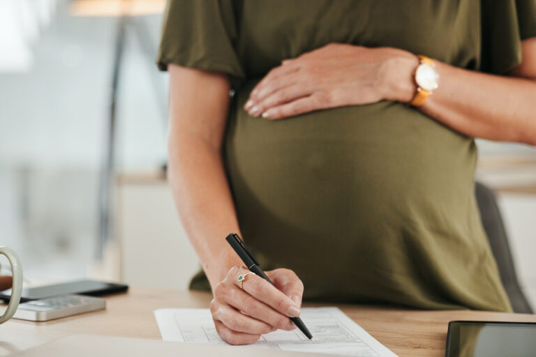 Businesswoman, pregnant and writing on document in office for information, maternity leave or insurance with contract. Female person, mother and hand on stomach for comfort, love and caring for baby.